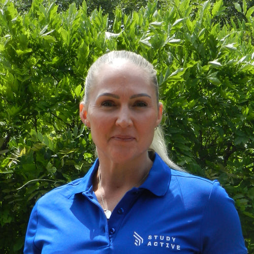 Person wearing a blue shirt with text standing outdoors in front of greenery