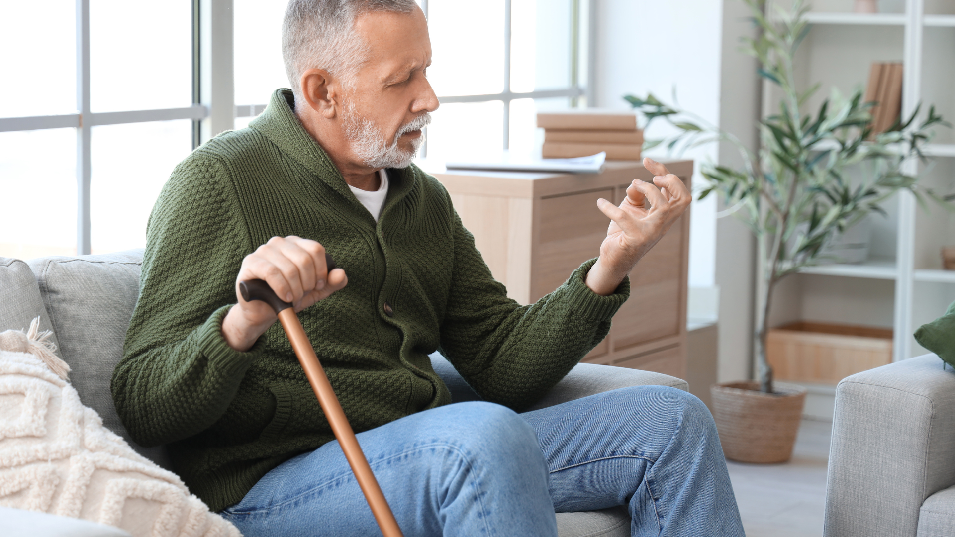 Image of a man with parkinsons disease siting on a sock with a walking cane in one and and his other had seizing up