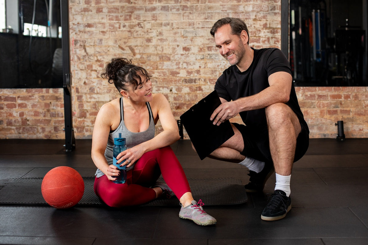 Study Active tutor observing a trainee coaching a client through a seated dumbbell press