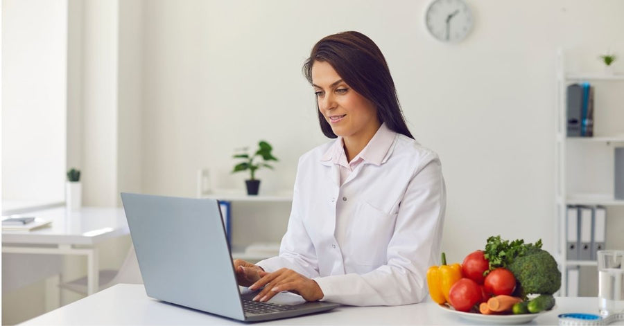 Nutrition coach working at a laptop beside fresh vegetables